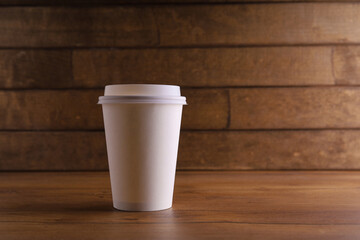 a paper cup of coffee on a wooden table with coffee beans