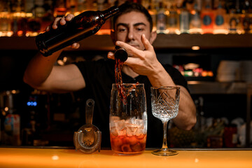 Accessories for making cocktail stands on the bar counter and bartender adds an ingredient to cocktail