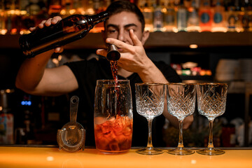 Tools for making cocktails and drinks stands on the bar counter and bartender adds an ingredient to mixing cup