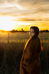 Fototapeta premium Beautiful woman drinking coffee in a field with sunset in the background