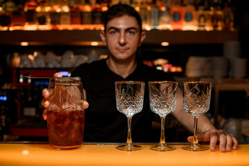 Young man, a professional bartender, holds in his hand tools for preparing and mixing alcoholic cocktails in a nightclub.