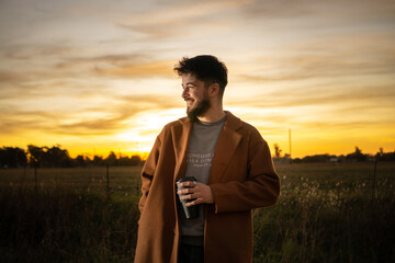 young man drinking coffee in the field with a sunset in the background