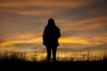 Beautiful woman drinking coffee in a field with sunset in the background