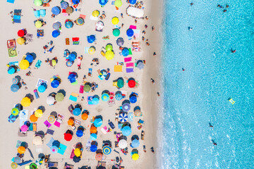 Aerial view of colorful umbrellas on sandy beach, swimming people in blue sea at sunset in summer. Sardinia, Italy. Tropical landscape with clear azure water. Travel and vacation. Top drone view