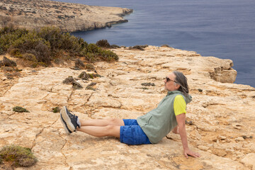 On a steep seashore sits a male traveler, Crete, Greece