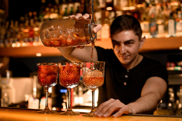 Bartender fills cocktail glasses with alcohol using measuring cup and strainer