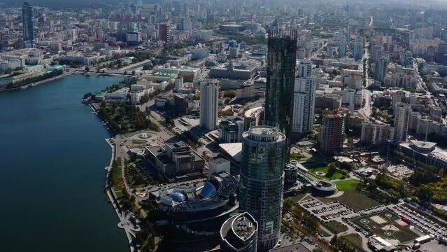 Top view of modern high-rise buildings in city panorama with river. Stock footage. Beautiful bird's-eye view of city on sunny day. Panorama of modern city with skyscrapers and river on sunny summer