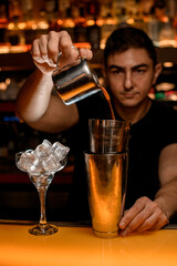 Bar counter with steel shaker cups and bartender pouring drink from copper mug into it