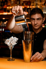Bartender pouring alcoholic drink from copper mug into steel shaker cups