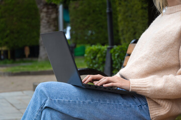 Close-up cropped shot of an unrecognizable young female freelancer typing on a laptop while sitting on a park bench