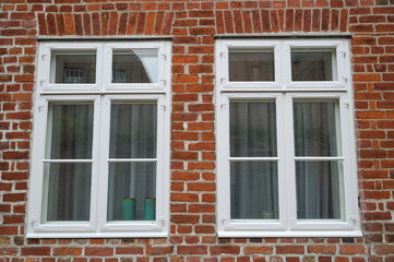Fototapeta na wymiar Zwei Fenster mit weißen Holzrahmen mit Sprossen in einer Hauswand aus Backstein