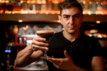 Barman serving glass with cold espresso martini cocktail in pub, closeup.