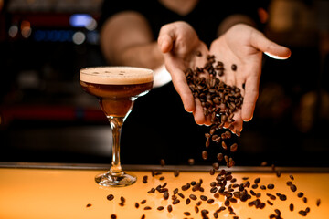 Barman pours out coffee beans to bar counter. Glass with martini espresso cocktail stands nearby