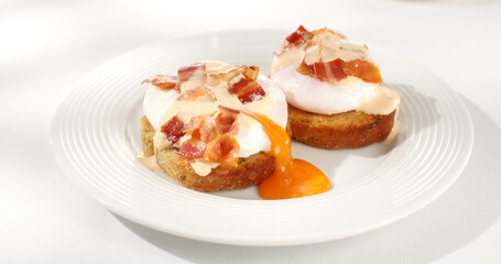 toast with poached egg and bacon on a plate. serving breakfast on a white background. sunny day. angle view. 