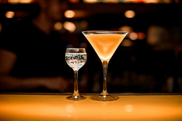 Glass of fresh yellow martini cocktail and glass with transparent bubble liquid nearby