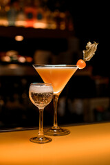 Bar counter with two alcoholic drinks: glass with champagne and fresh martini cocktail decorated with physalis fruit