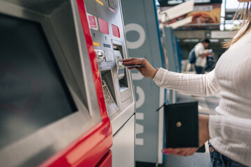 Unrecognizable young woman's hand inserting a banknote in the urban public transport card recharging machine.