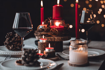 Rustic table decor for Christmas or New Year family dinner. Centrepiece with red candle, dry orange, cone, cinnamon, anise. Zero waste eco-friendly home. Cozy atmosphere, dark background. Close up