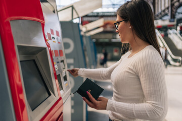 Young brunette woman's hand inserting paper money into public transport ticket vending machine.