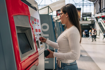 Young brunette woman's hand inserting a transit pass card into the machine to recharge her travel card.