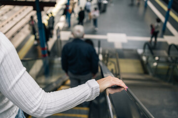 Hand of unrecognizable young woman's hand resting on escalator treadmill going down to subway.