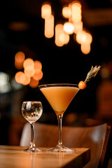 Table with ordered alcoholic drinks: glass with champagne and fresh martini cocktail decorated with physalis fruit