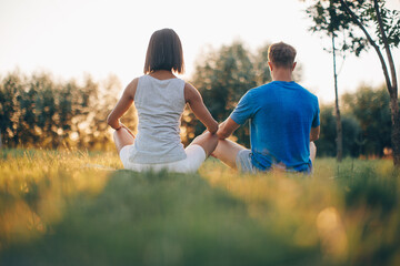 Young man and woman doing yoga as a couple outdoors. A couple doing acroyoga in the park.