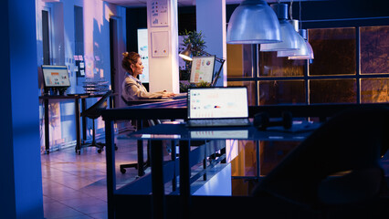 Young businesswoman checking online analytics in corporate office, planning business development at night. Female manager looking at financial graphs to create marketing report. Handheld shot.