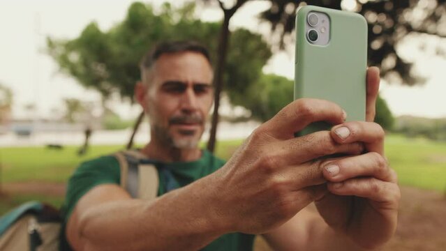 Middle-aged man takes photo on smartphone while standing in city park