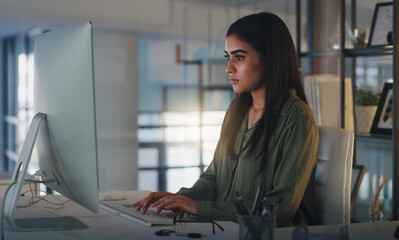 Computer, night and focus with a woman editor working in her office for a journalism or news report. Typing, editing and reporting with a young journalist at work on a desktop for online content