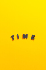 Three-dimensional black foam letters forming the word 'time' on a yellow background.