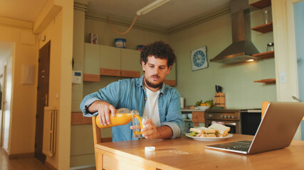 Guy dressed in denim shirt pours orange juice into glass and gets lunch in the kitchen