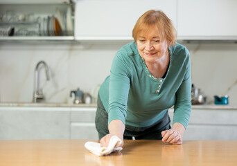 Senior female worker wipes table with rag and disinfects kitchen surface.Lady wiping messy dirty cooking counter for housekeeping housework or chores.