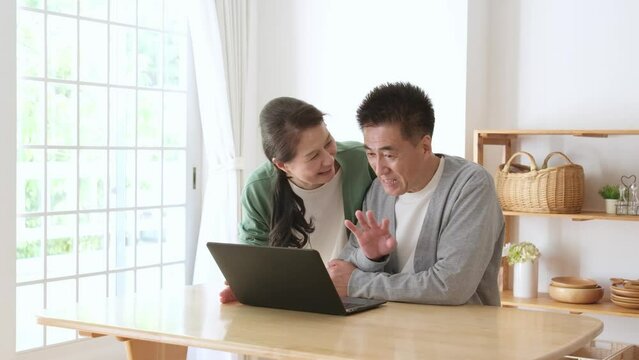 リビングでノートパソコンを使ってオンラインで会話をするシニア夫婦