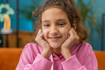 Close-up portrait of happy calm beautiful preteen school girl smiling friendly, glad expression looking at camera dreaming resting, relaxation feel satisfied good news. Young child kid at home room