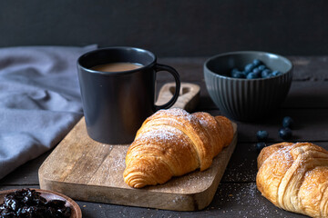 Coffee and croissant on a dark wooden background. French breakfast. 