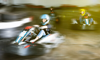 Group of glad cheerful positive people driving go-carts at racing track