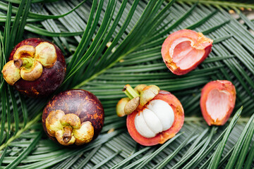 Fresh exotic fruits on green tropical palm leaves background. Sliced mangosteen. flat lay, overhead. Healthy food and diet concept. Top view.