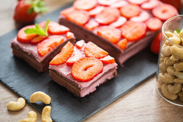 Cut of no baked cut raw cake made with dates, cashews and strawberries