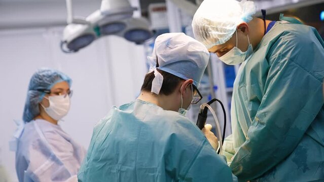 Rear view of a doctor performing operation. Surgeon uses a medical device in his work. Hospital staff at backdrop.