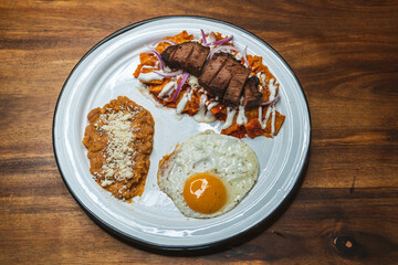Tasty breakfast - fried egg, chilaquiles with flank steak and refried beans