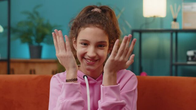 Portrait of Caucasian preteen school girl playing hide and seek peekaboo game, laughing. Young child, kid hiding and opening her face covering eyes with hands at home apartment sitting on orange couch