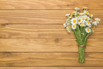 Small bouquet of chamomile flowers on wooden background, top view