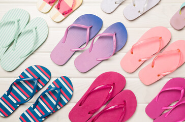 Many bright flip flops on wooden background, top view