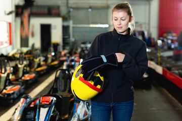 Glad cheerful positive pleasant woman with helmet standing near cars for motor racing in sport club