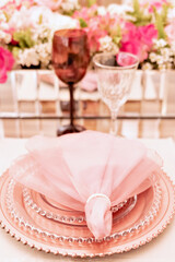 a table with a glass top, sousplat and pink napkins with an arrangement in the center