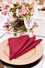 a table with a glass top, sousplat and pink napkins with an arrangement in the center