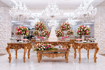 a golden wooden table, with a wedding cake in the center, decorated with vases of rose flowers and sweets