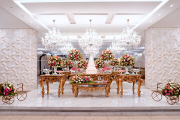 a golden wooden table, with a wedding cake in the center, decorated with vases of rose flowers and sweets
