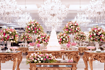 a golden wooden table, with a wedding cake in the center, decorated with vases of rose flowers and sweets